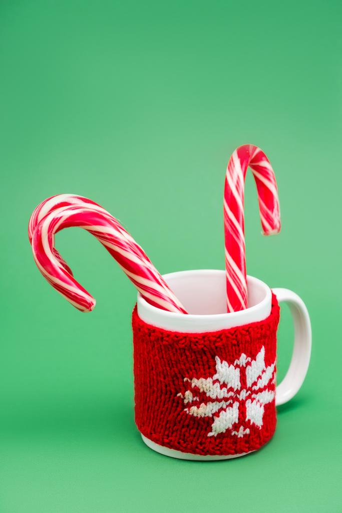 two candy canes in cup with knitted cup holder with snowflake on green background - Photo, Image