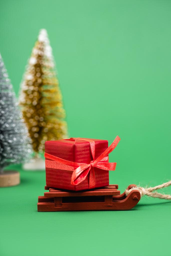 enfoque selectivo de plata y árboles de Navidad decorativos de oro cerca del trineo con caja de regalo en verde - Foto, imagen