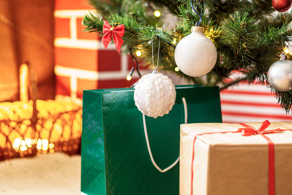 Kerstmis, winter, Nieuwjaar, Feestdag, Familie, Geschenkconcept - Vakantie sfeer thuis. Heldere presenteert dozen onder kerstboom versierd met ballen op de achtergrond rode open haard met brandend vuur - Foto, afbeelding