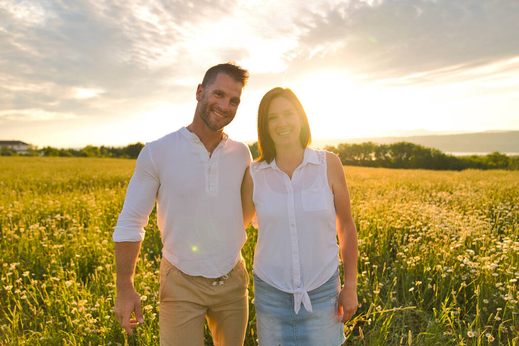 若いカップルが畑の夕焼けを背景にキスをして - 写真・画像