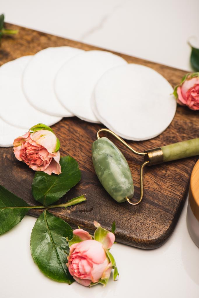 placa de corte com rolo de jade, almofadas de algodão e rosas de chá no fundo de mármore branco - Foto, Imagem