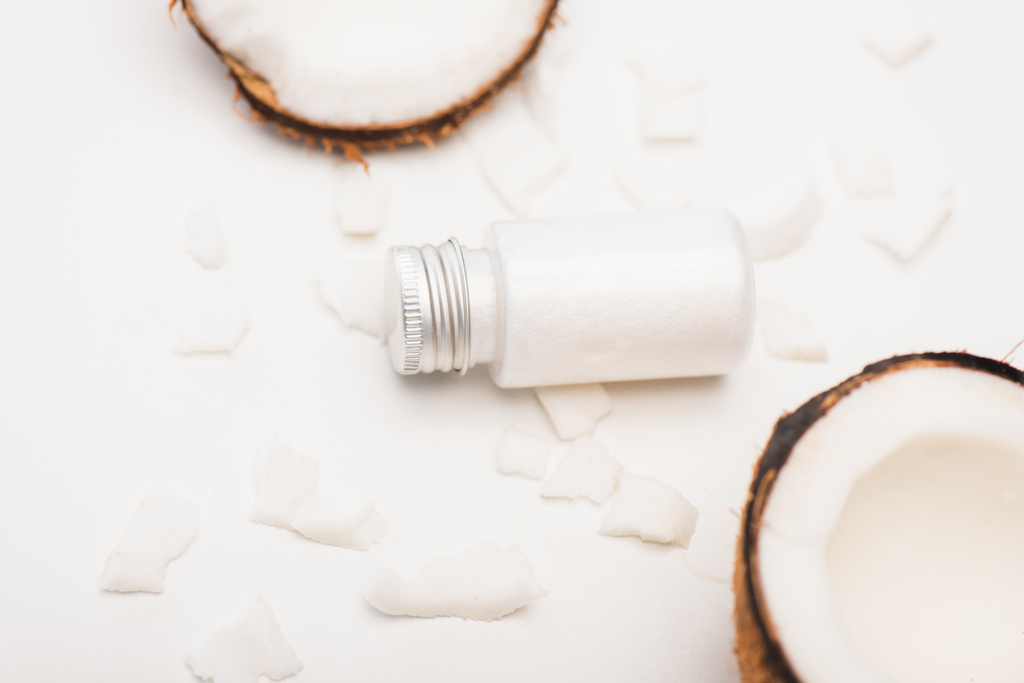 top of bottle with homemade lotion, coconut halves and flakes on white surface - Photo, Image