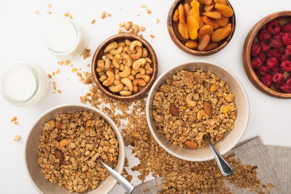 bovenaanzicht van heerlijke granola met noten, frambozen, yoghurt en gedroogde abrikozen geïsoleerd op wit - Foto, afbeelding