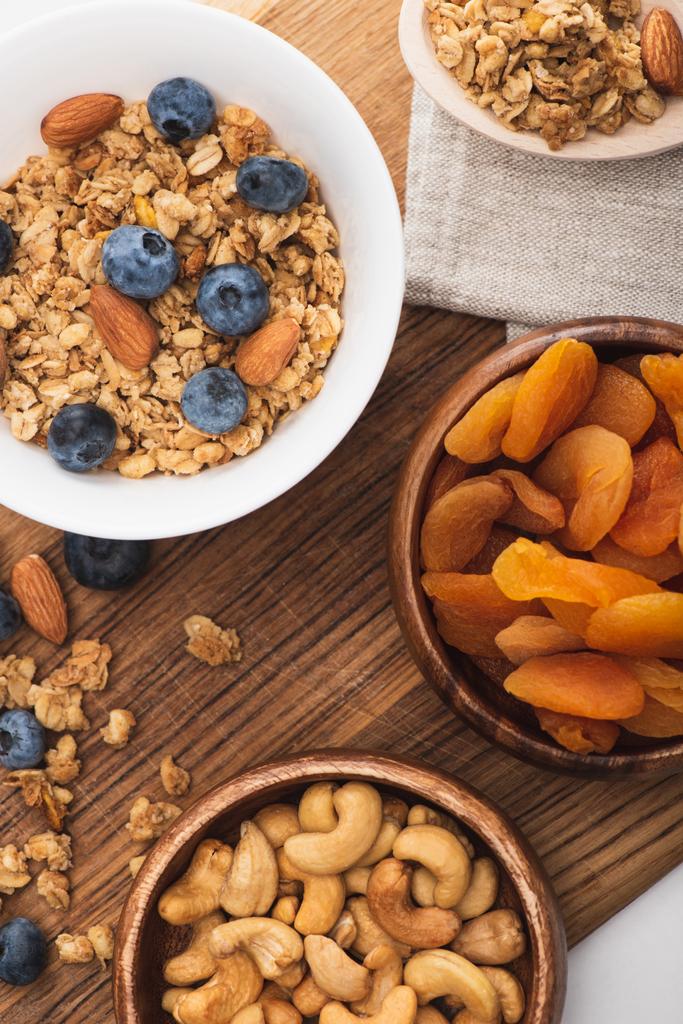 vrchní pohled na lahodnou granolu s ořechy, borůvkami a sušenými meruňky na dřevěné desce - Fotografie, Obrázek