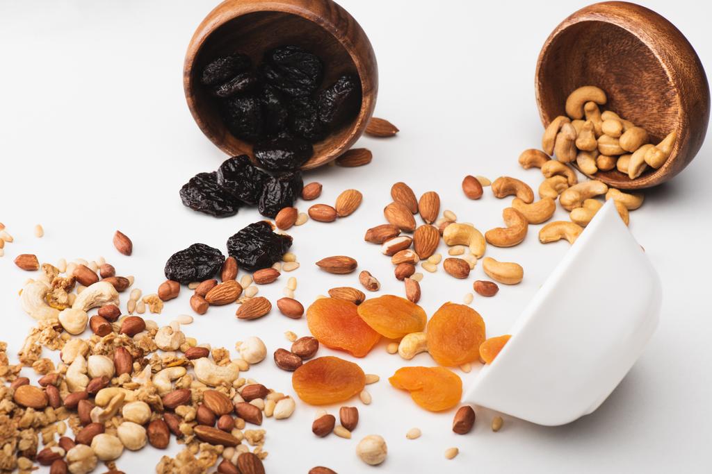 heerlijke granola met noten en gedroogde vruchten verspreid uit schalen op wit - Foto, afbeelding