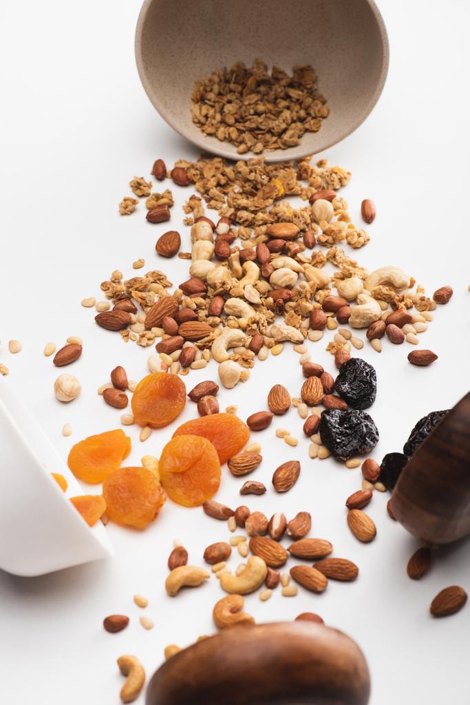 vynikající granola s ořechy a sušeným ovocem roztroušené z misek na bílém - Fotografie, Obrázek