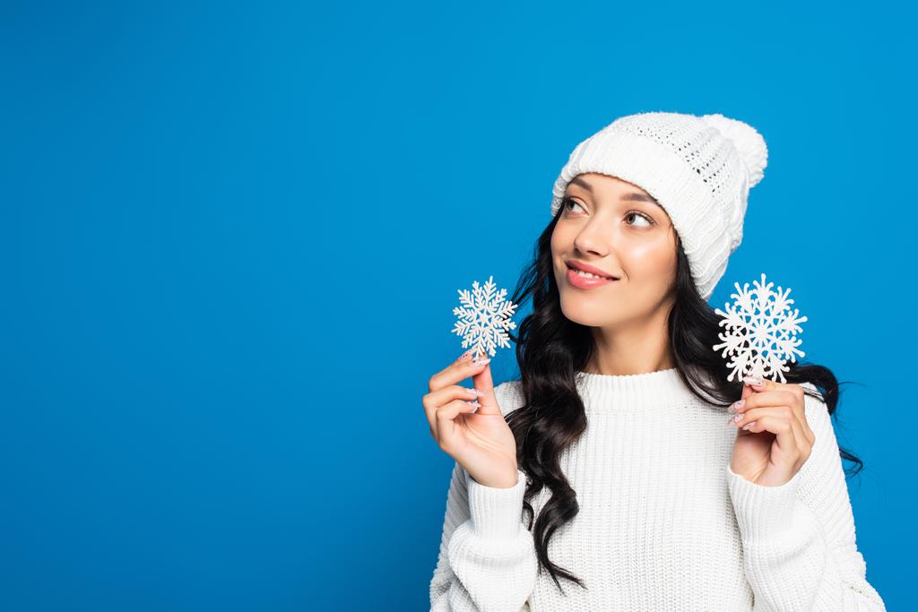 gioiosa donna in maglia cappello tenendo fiocchi di neve decorativi isolati su blu - Foto, immagini