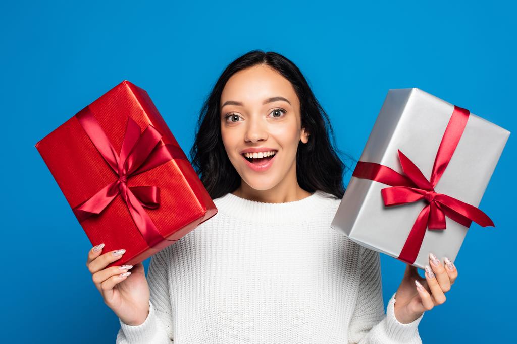 excited young woman in knitted sweater holding gift boxes isolated on blue - Photo, Image