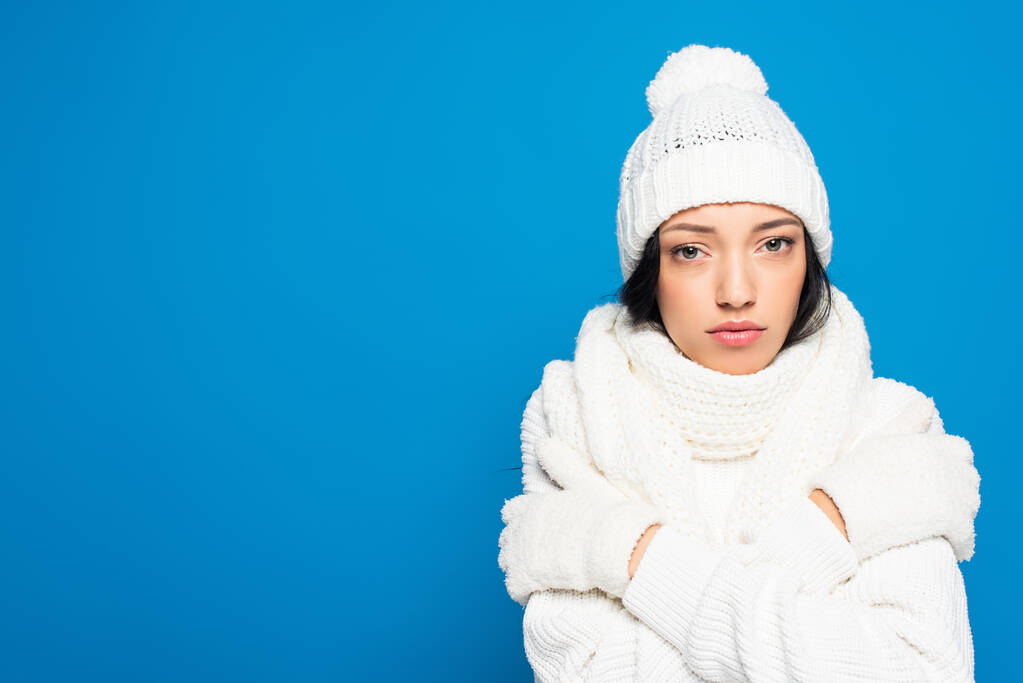 giovane donna scontenta in maglia cappello e guanti congelamento isolato su blu - Foto, immagini