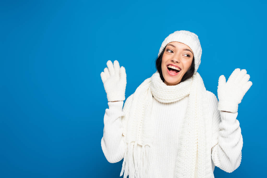 vzrušená žena v bílém zimním oblečení odvrací izolované na modré - Fotografie, Obrázek