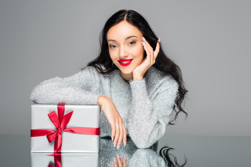 Mutlu bir kadın, kırmızı dudaklı, hediye kutusunun yanında, gri renkte. - Fotoğraf, Görsel