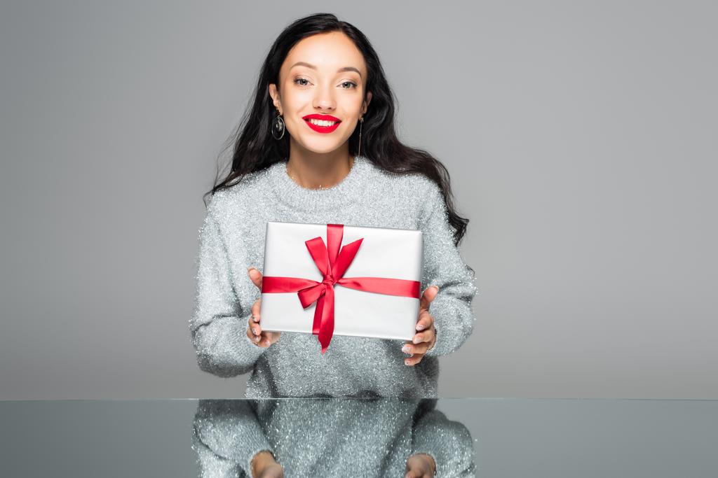 glückliche Frau mit roten Lippen hält Geschenkbox isoliert auf grau - Foto, Bild