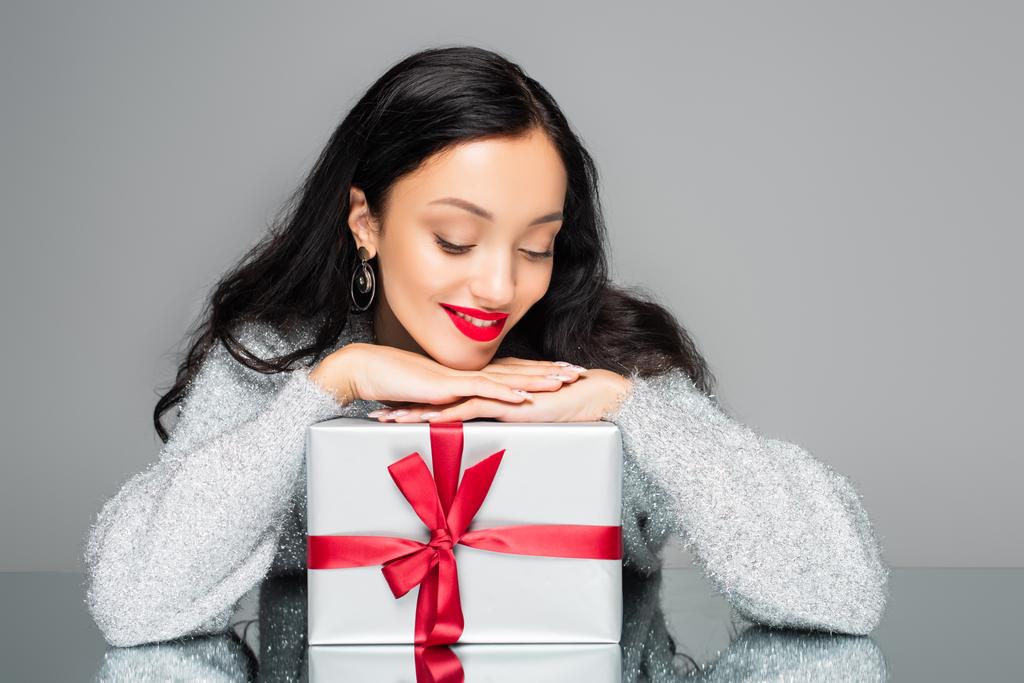 mujer feliz con labios rojos mirando caja de regalo aislado en gris - Foto, Imagen