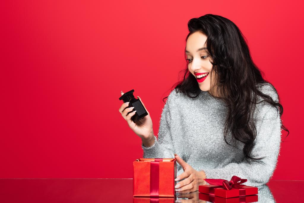 boldog nő gazdaság üveg parfüm közelében ajándék doboz elszigetelt piros - Fotó, kép