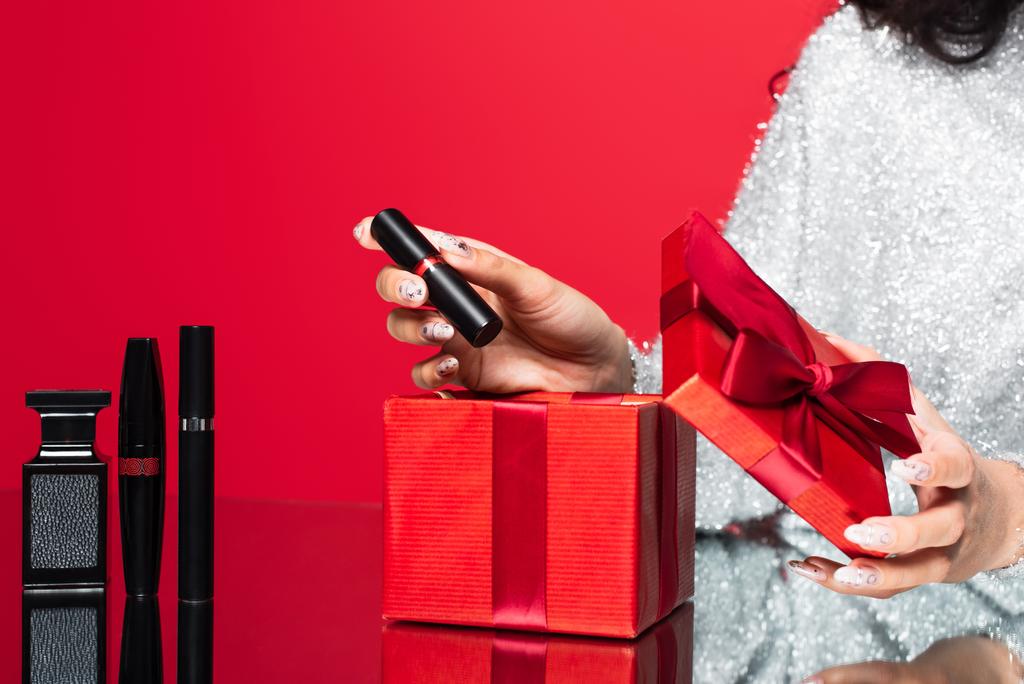 vista recortada de la mujer tomando lápiz labial de la caja de regalo cerca de cosméticos decorativos en rojo - Foto, imagen