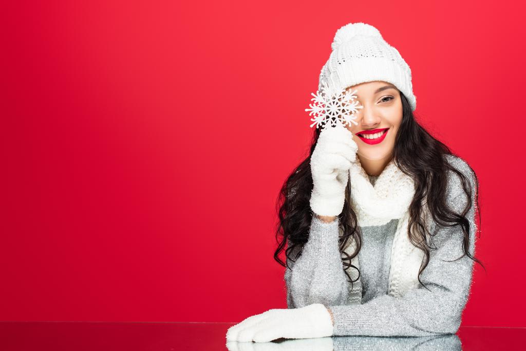 gelukkig vrouw in de winter outfit houden decoratieve sneeuwvlok geïsoleerd op rood - Foto, afbeelding