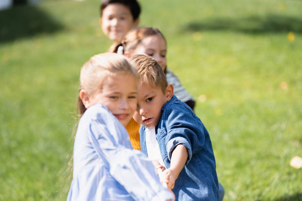 Poika vetää köyttä pelatessaan hinaaja sodan ystävien kanssa hämärtynyt etualalla puistossa  - Valokuva, kuva