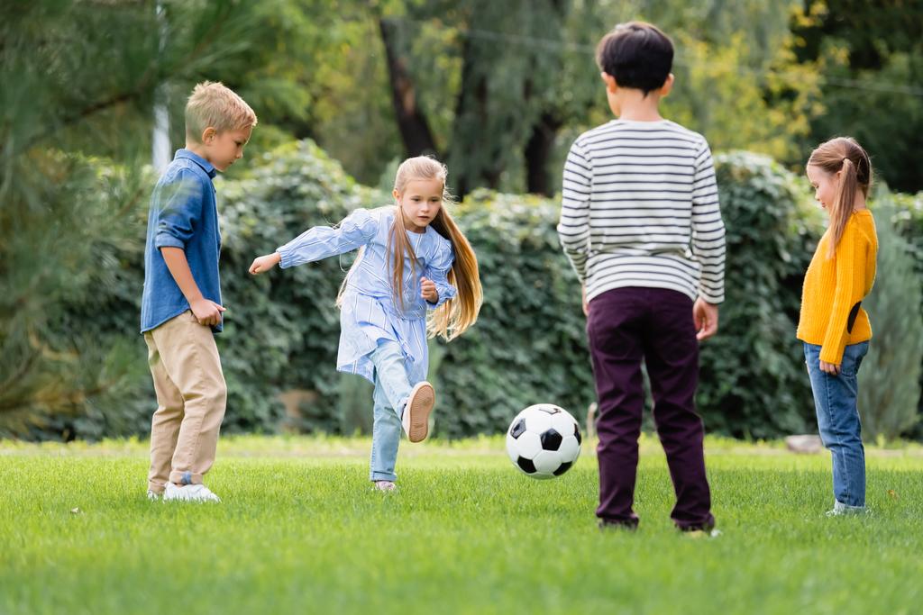 Девушка играет в футбол с друзьями на размытом переднем плане в парке  - Фото, изображение