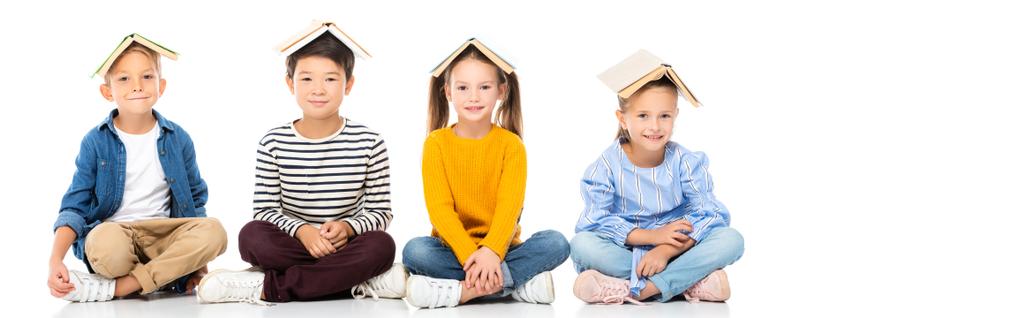 Pozitivní multikulturní děti s rukama na knihách sedících na bílém pozadí, prapor  - Fotografie, Obrázek