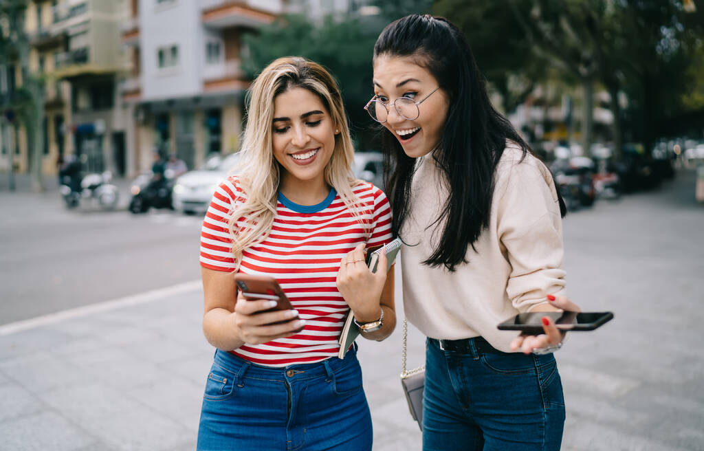 Emotional vielfältige Schüler beim Lesen empfangener E-Mails mit super guten Nachrichten, fröhliche Hipster-Mädchen beim gemeinsamen Zeitvertreib fürs Reisen zufrieden und Smartphone-Blogging überrascht mit 4g-Geschwindigkeit - Foto, Bild