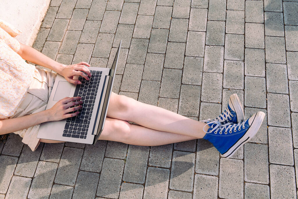 jalat tunnistamaton teini-ikäinen tyttö lenkkarit kirjoittamalla tietokoneen istuu lattialla kaupungin, käsite teknologian, nuorten ja kaupunkien elämäntapa, kopioi tilaa tekstiä - Valokuva, kuva