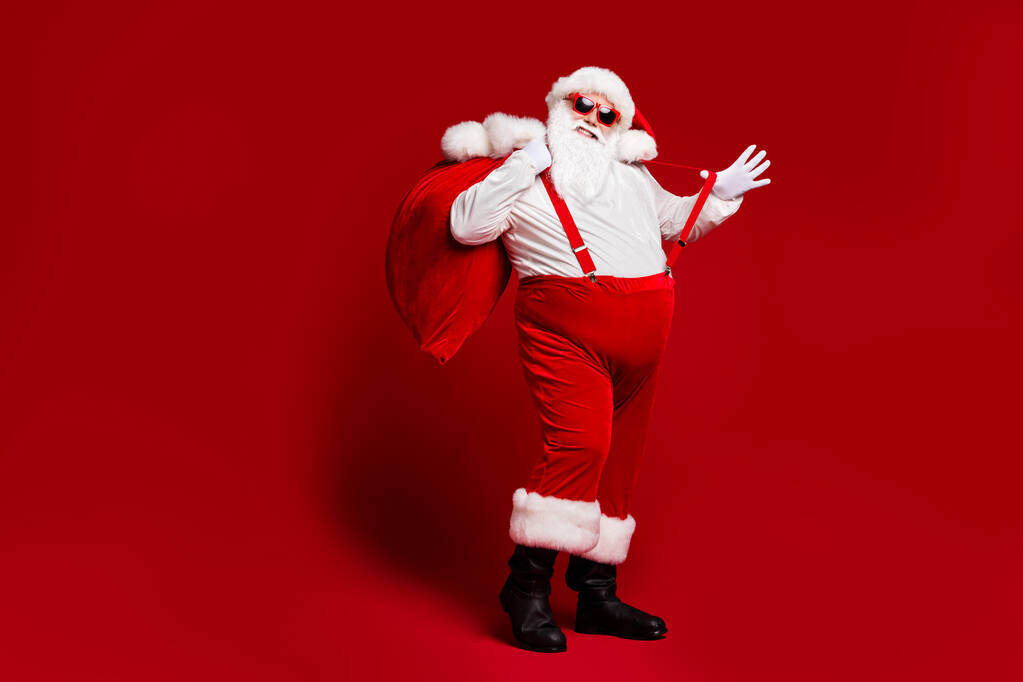 Полный размер тела вид его привлекательный веселый веселый веселый толстый Санта, несущий большой мешок, весело дурачась наслаждаясь изолированным ярким светом яркого красного цвета фона - Фото, изображение