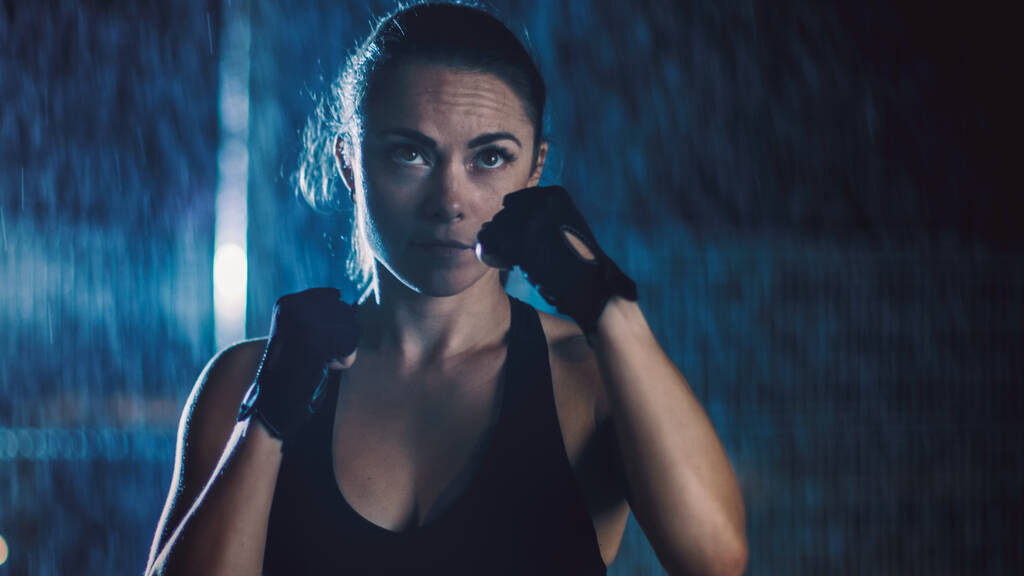 Piękna Sportowa dziewczyna fitness wykonuje ćwiczenia Sharowboxing. Ćwiczy w nocy w czasie ulewnego deszczu z jednym światłem za sobą.. - Zdjęcie, obraz