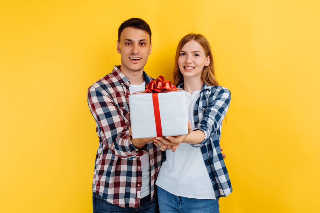 молодая пара в любви держит подарочную коробку на желтом фоне, День святого Валентина - Фото, изображение