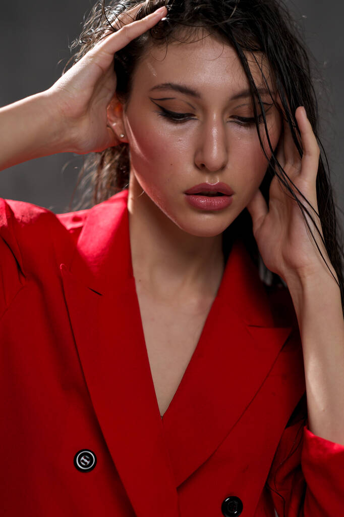 Młoda, piękna orientalna kobieta z długimi czarnymi włosami w czerwonej kurtce na czarnym tle. Modelka pozuje w studio. - Zdjęcie, obraz