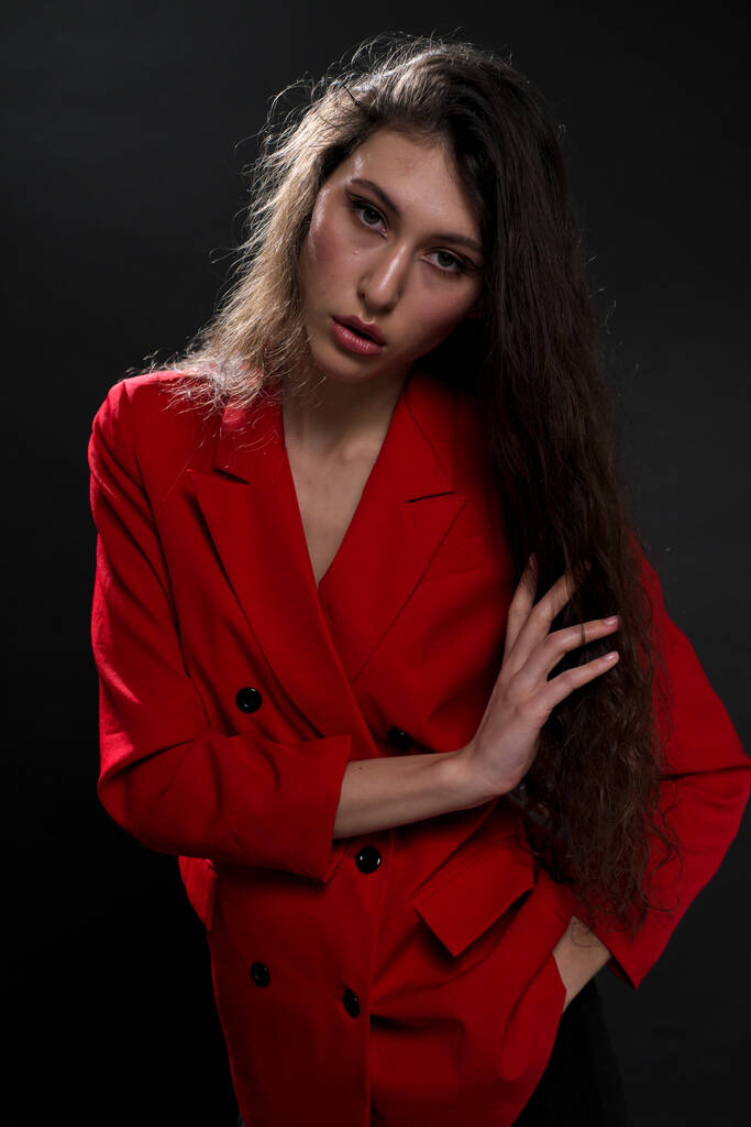 Una joven hermosa mujer oriental con el pelo largo y negro en una chaqueta roja sobre un fondo negro. La modelo posa en el estudio. - Foto, imagen