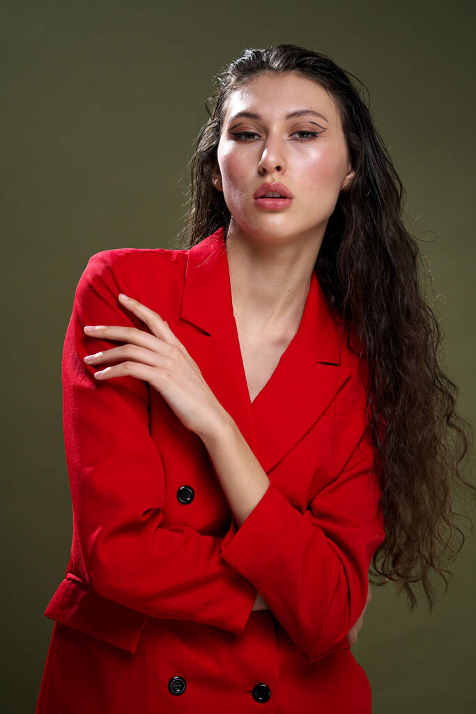 Egy érzéki fiatal nő portré piros kabátban, nedves, hosszú fekete hajjal, zöld háttérrel a stúdióban.. - Fotó, kép