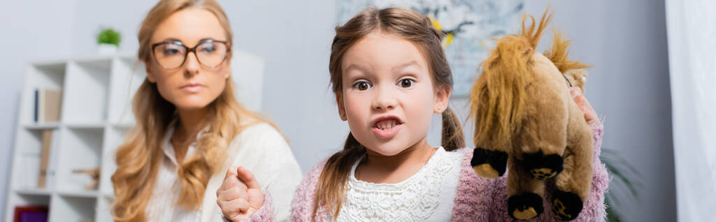 怒った女の子おもちゃを持つ患者と握りしめ拳を訪問心理学者、バナー - 写真・画像