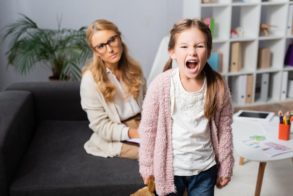 niña enojada con juguete gritando mientras visita al psicólogo - Foto, Imagen