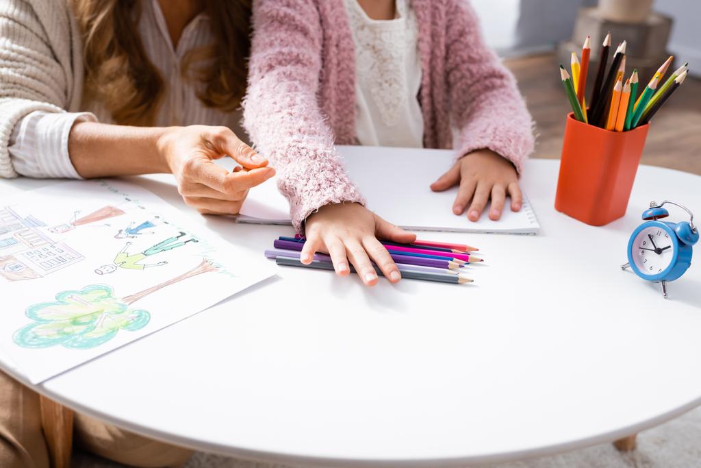 Ausgeschnittene Ansicht eines kleinen Mädchens, das beim Psychologen-Besuch Bilder mit bunten Bleistiften zeichnet - Foto, Bild