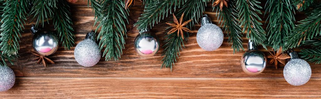 Top view of christmas balls, pine branches and anise stars on brown wooden background, banner - Photo, Image