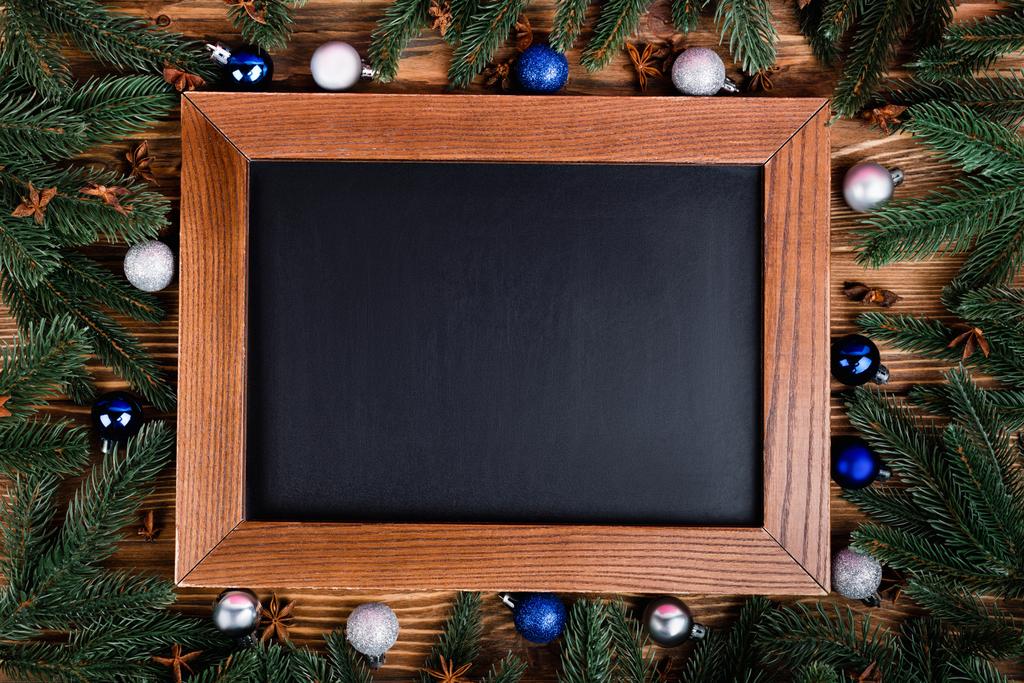 Vlak gelegd met blanco krijtbord, kerstballen, dennentakken en anijssterren op bruine houten ondergrond - Foto, afbeelding