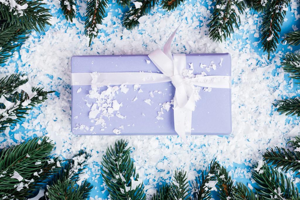 Top view of little gift box near pine branches and artificial snow on blue background - Photo, Image