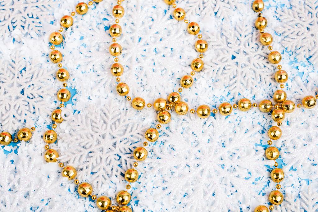 Крупный план золотых бусин с декоративными снежинками и искусственным снегом на синем фоне, новогодняя концепция - Фото, изображение