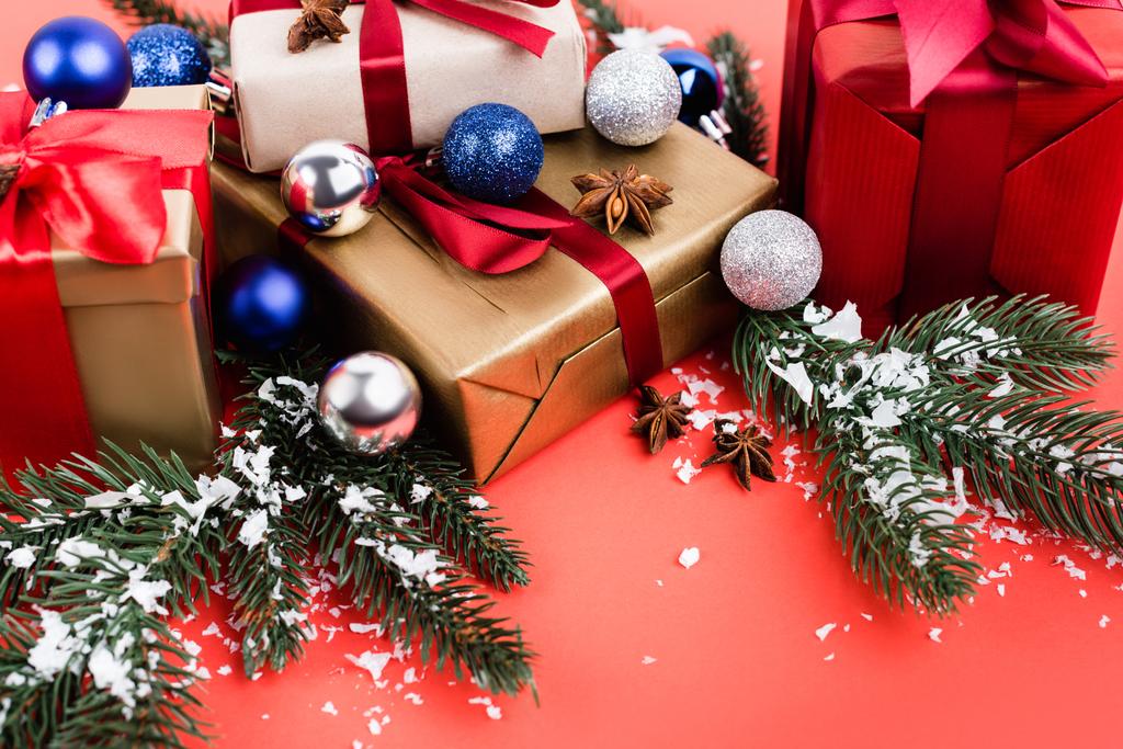 Cadeaux avec boules, étoiles d'anis, branches de pin et neige artificielle sur fond rouge - Photo, image