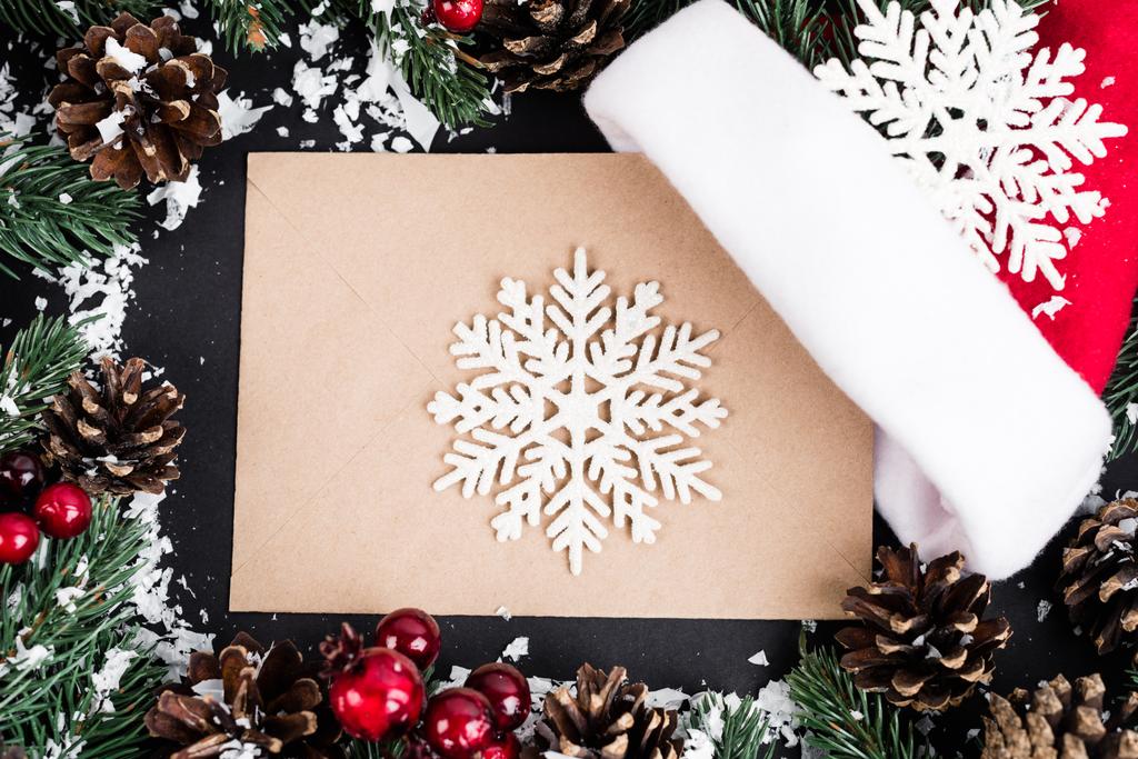 Top view of decorative snowflakes on envelope near pine cones, red beads and artificial snow on black background - Photo, Image