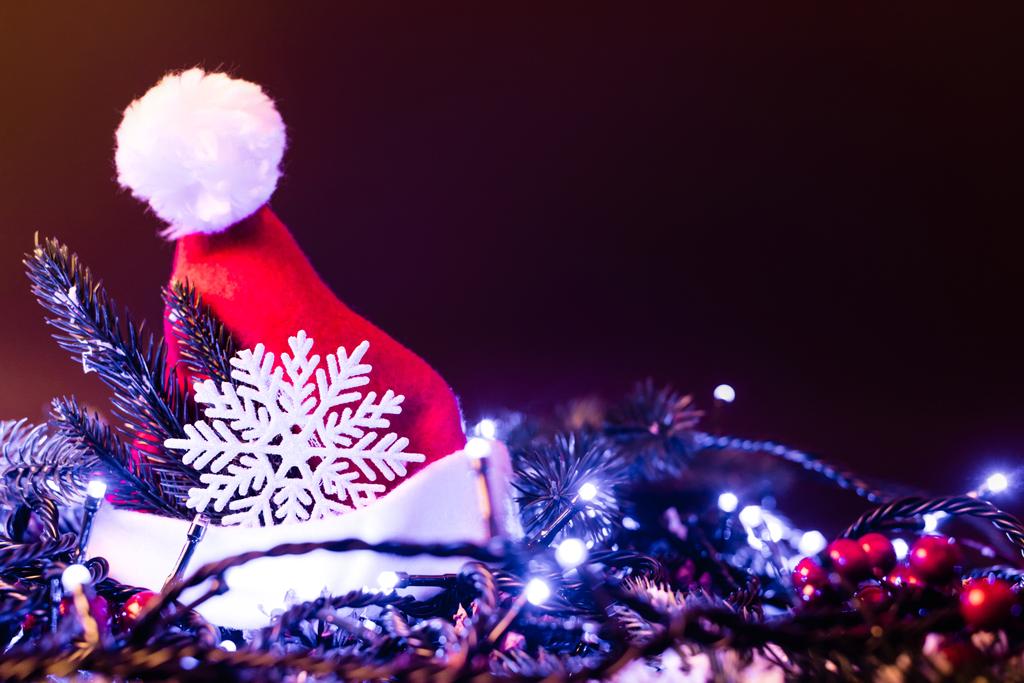 Felszíni szintje Mikulás kalap dekoratív hópelyhek, fenyő ágak és karácsonyi fények, újév koncepció - Fotó, kép
