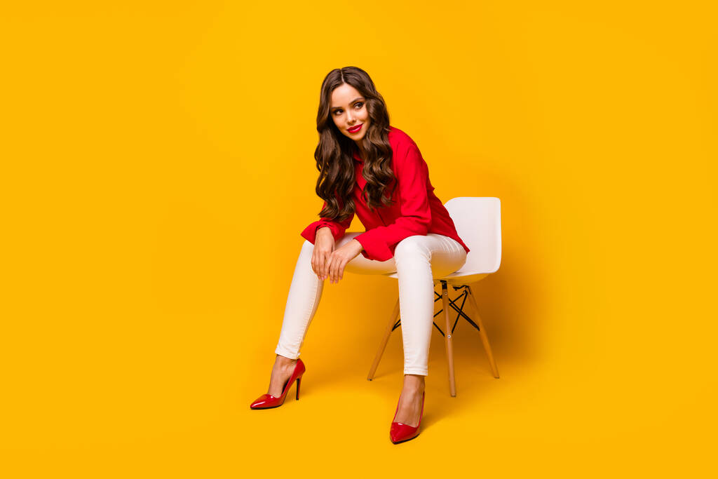 Teljes hosszúságú fotó vonzó elegáns üzleti hölgy ül főnökösködő kényelmes szék flörtölős hangulat nézd oldal üres tér kopás piros ing fehér nadrág magas sarkú elszigetelt sárga élénk szín háttér - Fotó, kép