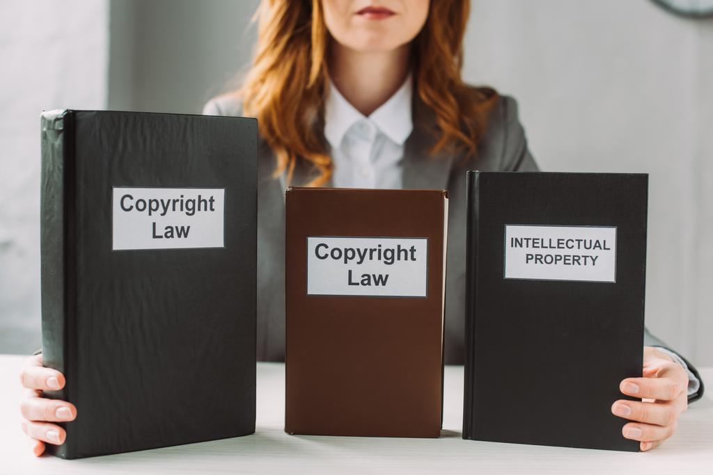 Обрезанный взгляд юриста, держащего книгу с надписью закона об интеллектуальной собственности и авторском праве на столе на размытом фоне - Фото, изображение