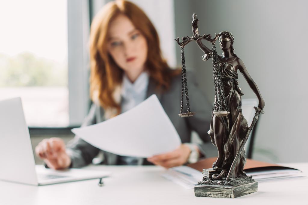 Figurka Themis na stole s rozmazaným právníkem pracujícím na pozadí - Fotografie, Obrázek