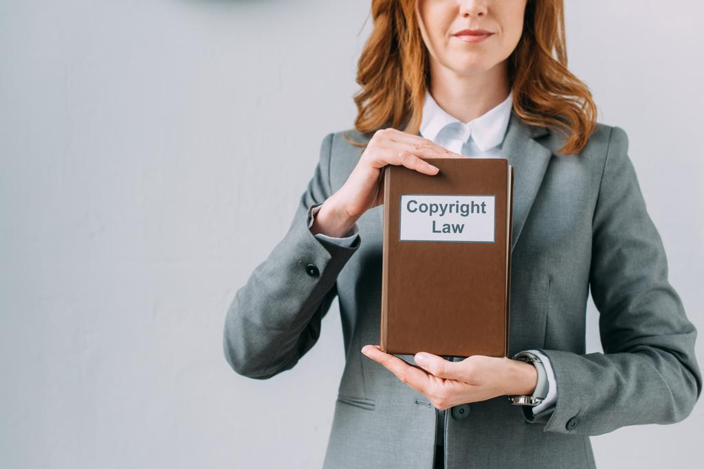 Ausgeschnittene Ansicht einer Rechtsanwältin, die Buch mit urheberrechtlichem Schriftzug auf grau zeigt  - Foto, Bild