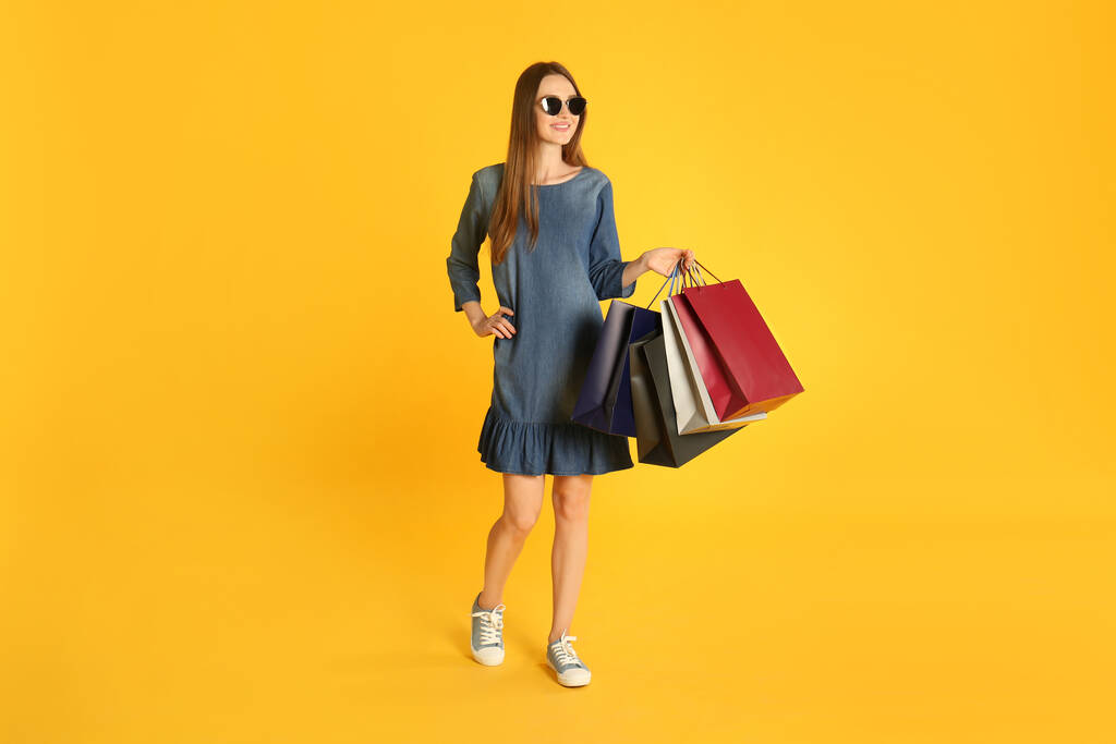 Gyönyörű fiatal nő papír bevásárló táskák sárga háttér - Fotó, kép
