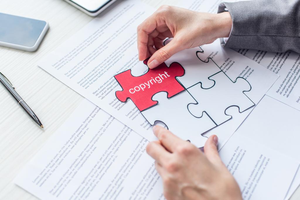Ausgeschnittene Ansicht einer Rechtsanwältin, die mit Papierblättern ein rotes Puzzle mit urheberrechtlichen Schriftzügen am Arbeitsplatz platziert - Foto, Bild