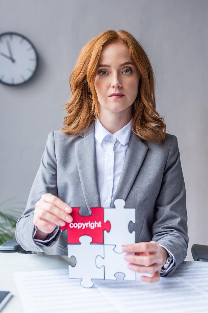 Serious lawyer looking at camera, while showing jigsaw puzzles with copyright lettering at workplace on blurred background - Photo, Image