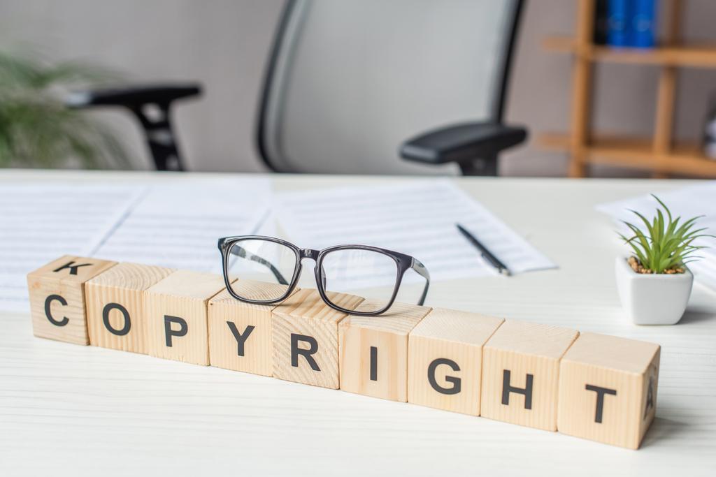 Großaufnahme von Brillen auf Holzwürfeln mit Urheberrechtsbeschriftung mit verschwommenem Arbeitsplatz auf dem Hintergrund - Foto, Bild