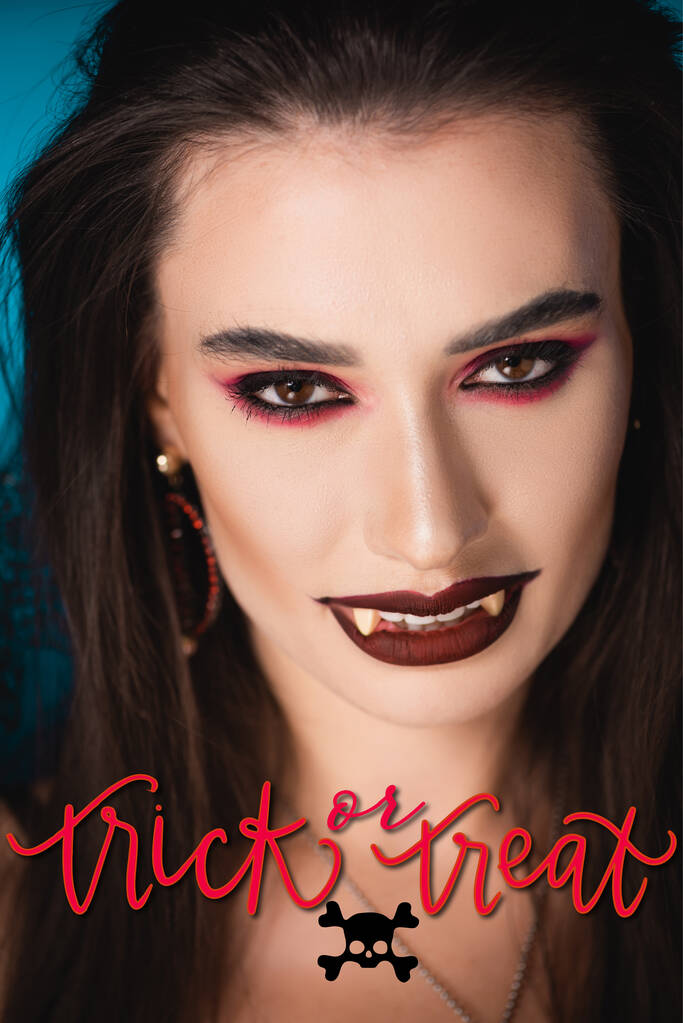 wampir z czarnym makijażem i białe straszne zęby patrząc na aparat w pobliżu trick lub leczyć liternictwo  - Zdjęcie, obraz